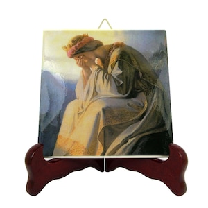May include: A ceramic tile with a painting of a woman wearing a crown and a white robe, sitting on a rock and crying. The tile is on a wooden stand.