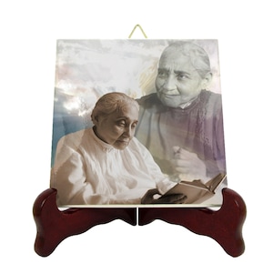 May include: A ceramic tile with a picture of two women. The woman in the foreground is reading a book. The woman in the background is a faded image. The tile is on a wooden stand.
