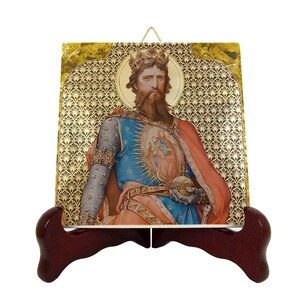 May include: A decorative tile featuring a regal figure with a crown, beard, and ornate clothing. The image is set against a gold patterned background and displayed on a dark wooden stand. The figure is wearing a blue tunic and red cape.