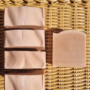 Peut inclure: Vue de six savons roses clairs de forme rectangulaire. Cinq savons présentent une texture ondulée, tandis que le sixième a une surface lisse. Les savons sont disposés sur une surface tissée marron clair.