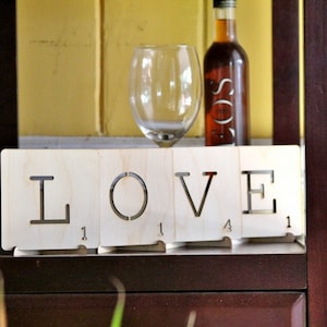 May include: Wooden block letters spelling "LOVE" with the number "1" on each block. The letters are on a shelf with a glass wine glass and a bottle of wine.