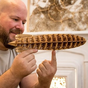 May include: A man holds a wooden model of a ship, the model is detailed and intricate, with many small pieces of wood.