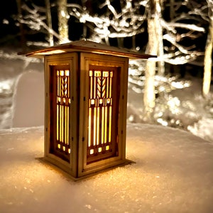 May include: A wooden lantern with a geometric design and a warm glow, sitting on a snowy surface.
