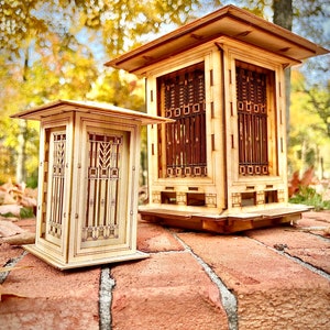 May include: Two wooden model houses with intricate window designs. The larger house has a square base and a pitched roof. The smaller house has a rectangular base and a flat roof. Both houses are made of light wood and have a natural finish.