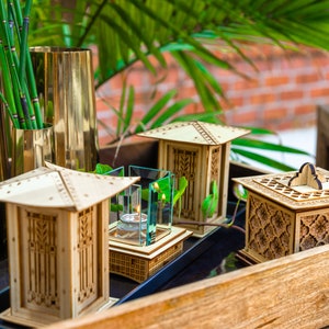 May include: Three wooden decorative boxes with intricate designs, one with a glass top and a small candle inside, on a wooden tray.