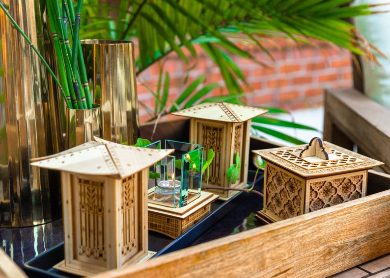May include: Three wooden decorative boxes with intricate designs, one with a glass top and a small candle inside, on a wooden tray.