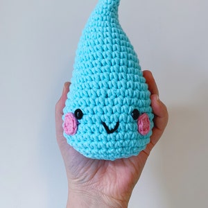 Può includere: Una goccia di pioggia all'uncinetto blu chiaro con un viso sorridente e guance rosa.