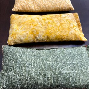 May include: Three rectangular pillows in a row. The top pillow is yellow with a repeating leaf pattern. The middle pillow is yellow with a floral design. The bottom pillow is green with a textured pattern.