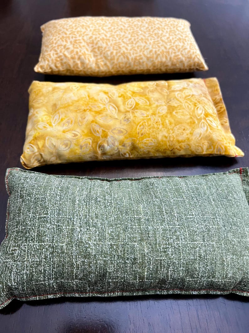 May include: Three rectangular pillows in a row. The top pillow is yellow with a repeating leaf pattern. The middle pillow is yellow with a floral design. The bottom pillow is green with a textured pattern.