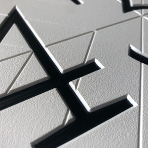 close up view that shows the details of the sign. The black, modern numbers are recessed into the white geometric background. There is a clean chamfered edge around the profile of the numbers. The quality looks professional and precise.