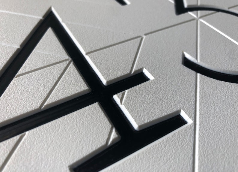 close up view that shows the details of the sign. The black, modern numbers are recessed into the white geometric background. There is a clean chamfered edge around the profile of the numbers. The quality looks professional and precise.