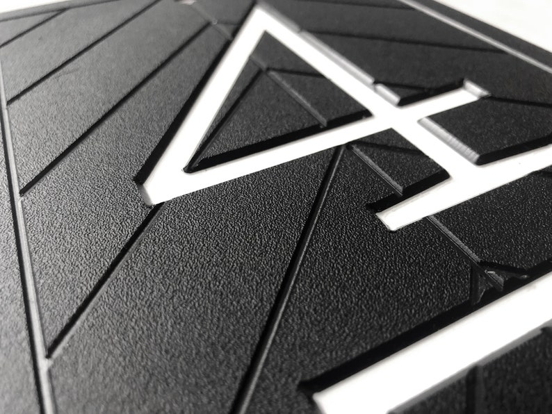 Close up image showing the details of the sign. The white, modern numbers are recessed into the black geometric background. There is a clean chamfered edge around the profile of the numbers and an embossed texture on the surface of the sign.