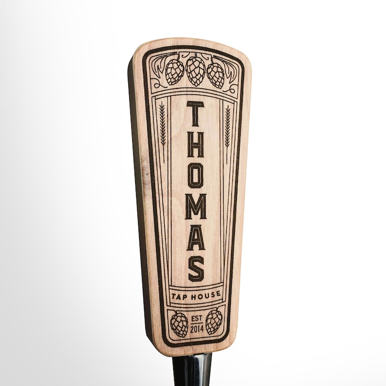 May include: A wooden beer tap handle with the name "THOMAS TAP HOUSE EST 2014" engraved on it. The handle is decorated with hops and wheat.