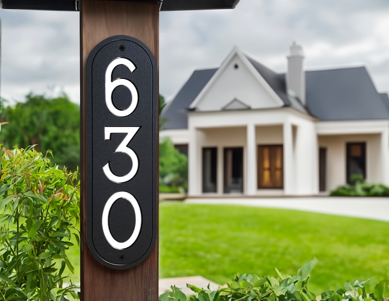 May include: Black and white house number plaque with the numbers 630 on a wooden post. The plaque is oval shaped and has a modern design.