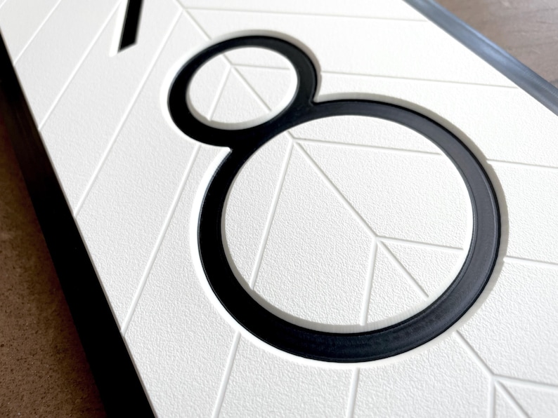 close up view that shows the details of the sign. The black, modern numbers are recessed into the white geometric background. There is a clean chamfered edge around the profile of the numbers. The quality looks professional and precise.