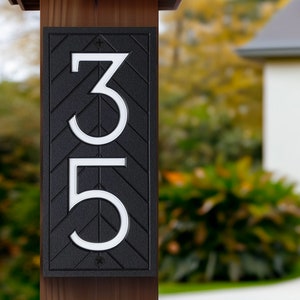 May include: Black house number sign with white numbers 3 and 5. The sign is mounted on a wooden post.