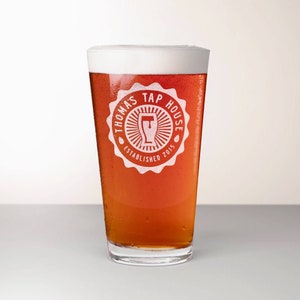 Tapered, pub style, beer glass features an etched design placed slightly above the center of the glass. The design is circular with a scalloped frame. within the frame, a beer glass icon inside a round sunburst design is surrounded by customized text