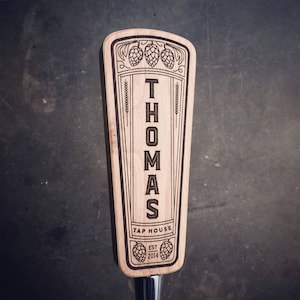 May include: A wooden beer tap handle with the name "Thomas Tap House" and the year "2014" engraved on it. The handle is decorated with a stylized design of hops and wheat.