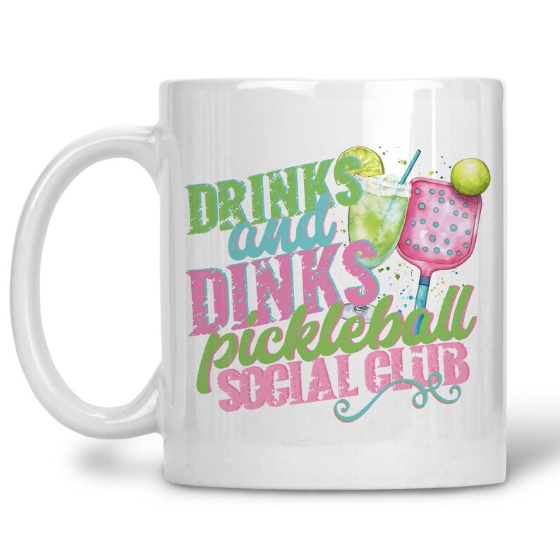 May include: White ceramic mug with the words "DRINKS and DINKS pickleball SOCIAL CLUB" in green, blue, and pink. The mug features a watercolour illustration of a cocktail, pickleball paddle, and lime.