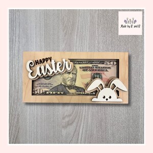 May include: A wooden Easter-themed decoration featuring a fifty-dollar bill. The words "Happy Easter" are cut out of white wood and placed above the bill. A white and tan bunny is on the right side of the bill.