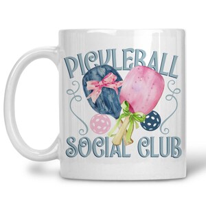 May include: White ceramic mug with a watercolour design. The mug features the text "Picklerball Social Club" and illustrations of pickleball paddles, balls, and decorative swirls in blue, pink, and green.