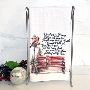 May include: A white kitchen towel with a watercolor illustration of a red cardinal perched on a lamppost next to a wooden bench with presents. The text reads "Christmas in Heaven What will they do? They'll come down to Earth to spent it with you. Save them a seat just one empty chair, you may not see them but they will be there."