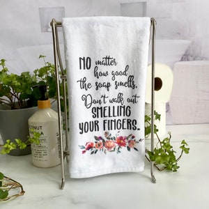 May include: White kitchen towel with a floral design and the text "NO matter how good the soap smells, Don't walk out SMELLING YOUR FINGERS."