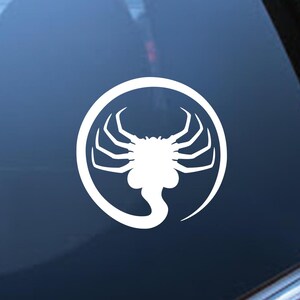 May include: White vinyl sticker of an alien creature with a circle around it. The creature has a long tail and eight legs.