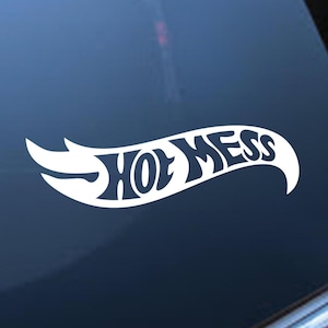 Könnte beinhalten: Weißer Vinyl-Aufkleber mit dem Text "Hot Mess" in einer stilisierten Schriftart, eingebettet in ein geschwungenes, flammenartiges Design. Geeignet für die Anbringung auf einer Autoscheibe oder anderen glatten Oberflächen.