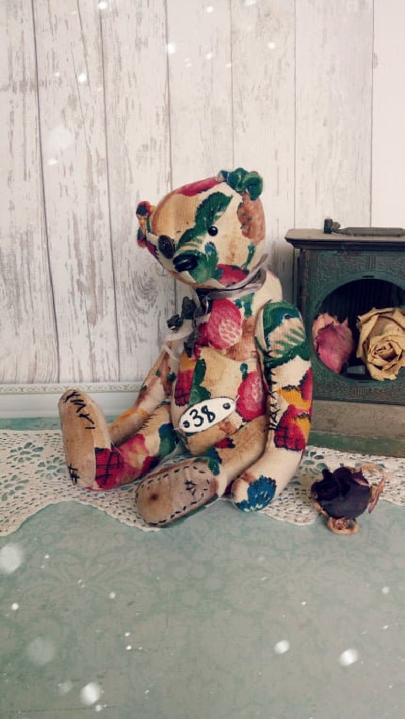 May include: A handmade teddy bear with a floral fabric pattern. The bear is sitting on a white lace doily and has a tag with the number "38" on its chest.