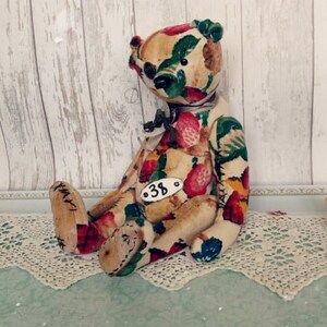 May include: A handmade teddy bear with a floral print fabric. The bear is sitting on a white lace doily. The bear has a tag with the number "38" on it.