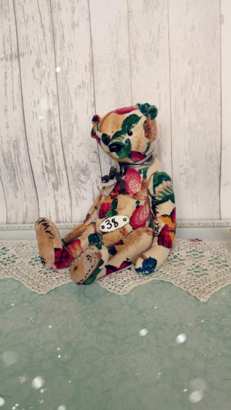 May include: A handmade teddy bear with a floral print fabric. The bear is sitting on a white lace doily. The bear has a tag with the number "38" on it.