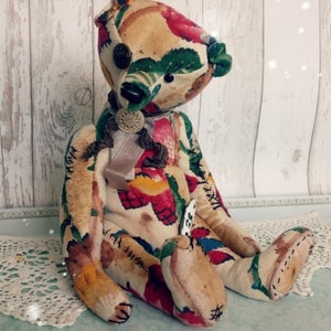 May include: A handmade teddy bear with a floral fabric pattern in shades of red, yellow, green, and blue. The bear has a stitched-on bow and a tag with the number "72" on it.