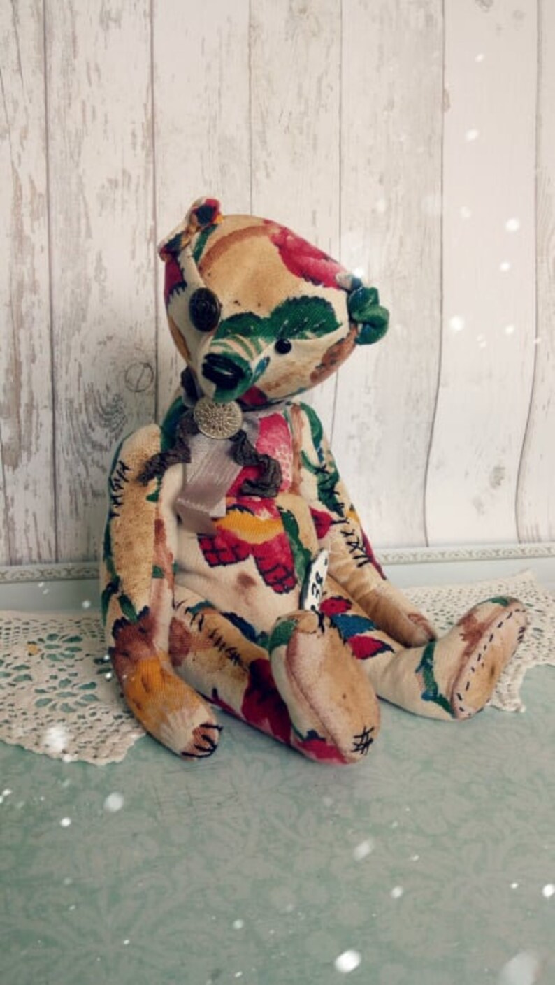 May include: A handmade teddy bear with a floral fabric pattern in shades of red, yellow, green, and blue. The bear has a stitched-on bow and a tag with the number "72" on it.