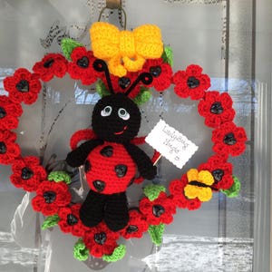 May include: A crocheted ladybug wreath with red and green leaves, a yellow bow, and a sign that says "Ladybug Hugs".