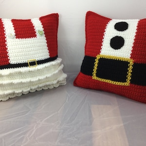 May include: Two crocheted pillow covers, one red with a white belt and black buckle, and the other white with a red bodice and a black belt. Both pillows have a white ruffle trim.