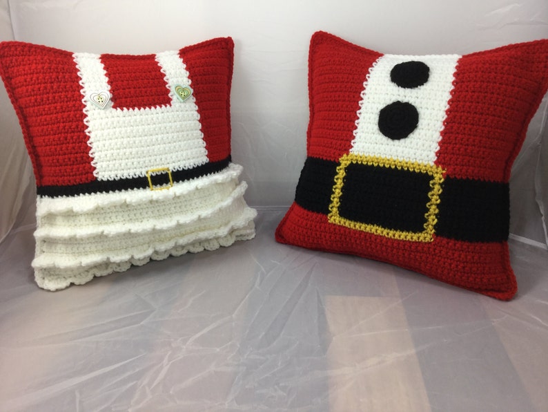 May include: Two crocheted pillow covers, one red with a white belt and black buckle, and the other white with a red bodice and a black belt. Both pillows have a white ruffle trim.