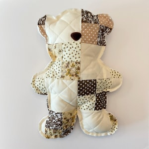 Könnte beinhalten: Ein gesteppter Teddybär im Patchwork-Design. Der Bär besteht aus cremefarbenen, braunen und beigefarbenen Stoffen mit Blumen- und Tupfenmustern. Er hat eine braune Knopf-Nase und ist ca. 30 cm groß.