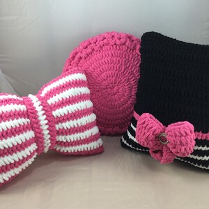 May include: Three crocheted cushions, one pink and white striped, one pink with a round shape, and one black with a pink bow.