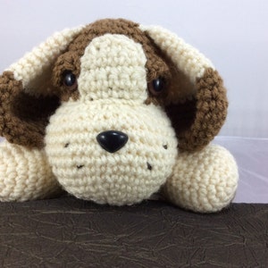 May include: A crocheted stuffed dog toy with brown and white fur. The dog has a black nose and brown eyes.