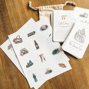 May include: A set of printable cards with watercolor illustrations and Bible verses. The cards feature a variety of images, including a sheep, a tree, a hand, and a mountain. The text on the cards includes the verses "Lost Sheep" and "The Jesus Tree".