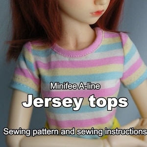 May include: A striped pink, yellow, and blue jersey top sewing pattern for dolls. The pattern is called "Minifee A-Line Jersey Tops" and includes sewing instructions.