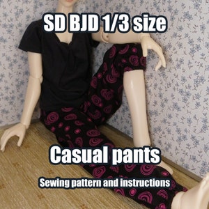 Op de afbeelding: Een naaipatroon en instructies voor het maken van een casual broek voor een SD BJD pop in maat 1/3. De broek is zwart met roze en witte cirkels.
