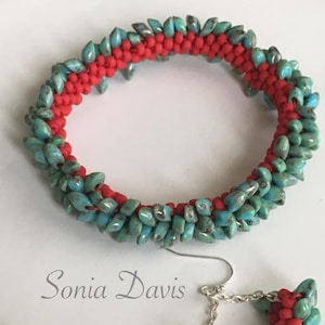 Op de afbeelding: Een set turquoise en rode kralen sieraden, bestaande uit een armband en een paar oorbellen. De armband is een cirkel van kralen, terwijl de oorbellen halvemaanvormig zijn. De kralen zijn gerangschikt in een patroon van afwisselend turquoise en rood.