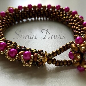 May include: A pink and gold beaded bracelet with a flower-shaped clasp. The bracelet is made with small seed beads and larger round beads. The clasp is made with a single large iridescent bead in the center.