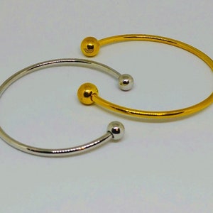 以下が含まれることがあります： ボールのアクセントが付いた、ゴールドとシルバーのシンプルなバングルブレスレット2本