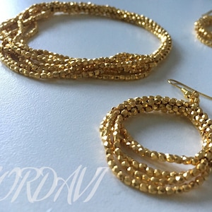 May include: A set of gold-toned beaded jewelry, including a necklace and a pair of earrings. The necklace and earrings are made of multiple strands of small, faceted beads.