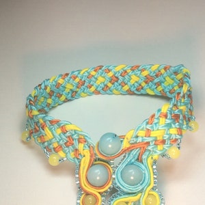 May include: A woven bracelet with blue, yellow, and orange threads. The bracelet has a decorative design with turquoise beads and yellow beads.