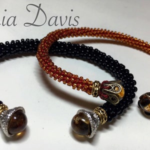 May include: Two beaded bracelets with decorative metal and stone accents. One bracelet is black and the other is orange and brown.