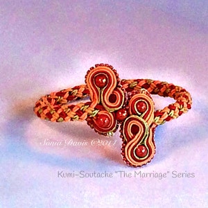May include: A red and orange braided bracelet with a decorative knot in the center. The knot is made of red and orange soutache braid and features a red bead in the center. The bracelet is called "The Marriage" Series.